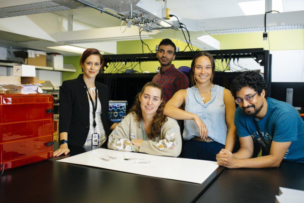 5 people in a lab standing around a table smiling.